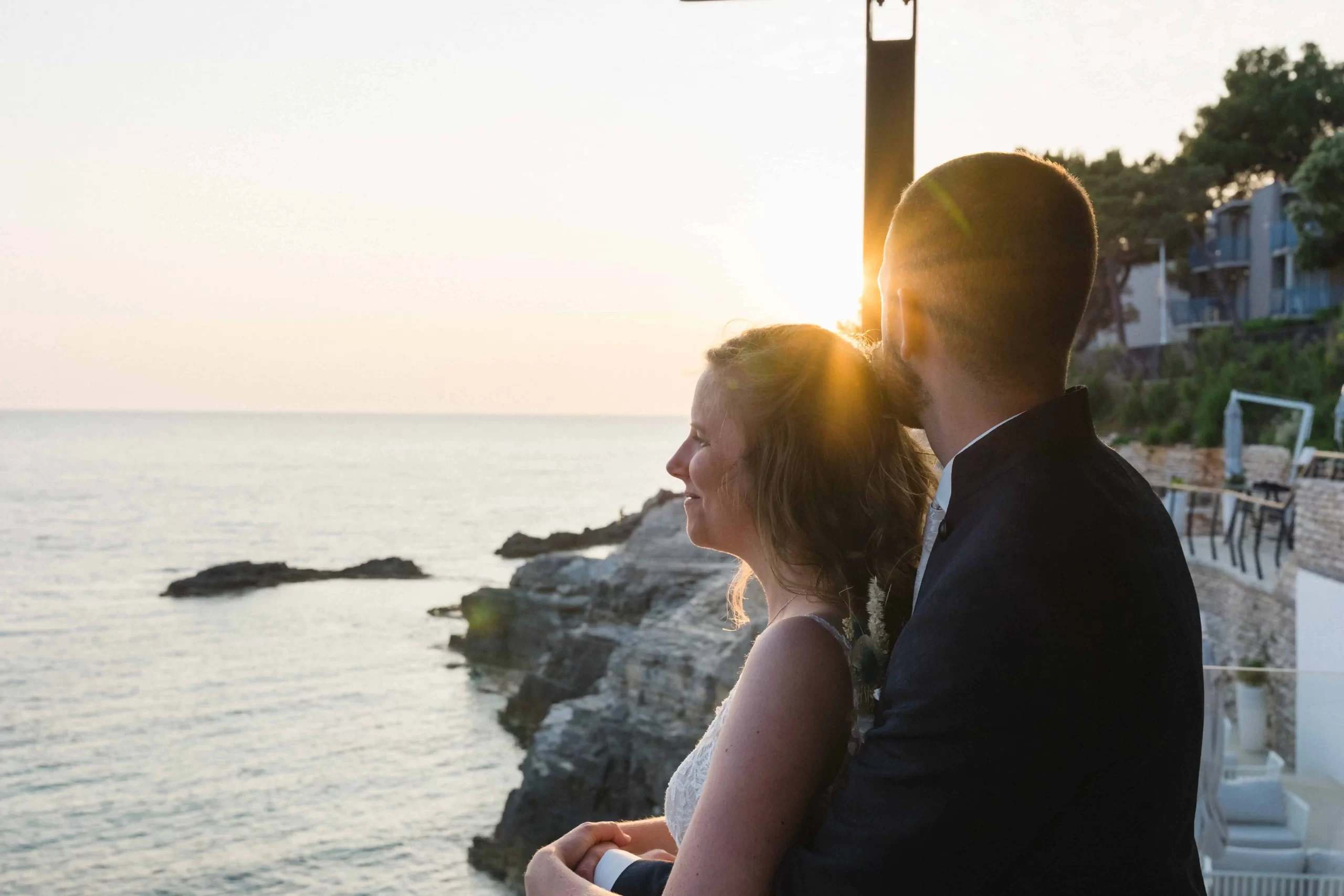 Romantic bride and groom embrace during sunset on a rocky beach in Pula, Istria, Croatia, captured by a wedding photographer