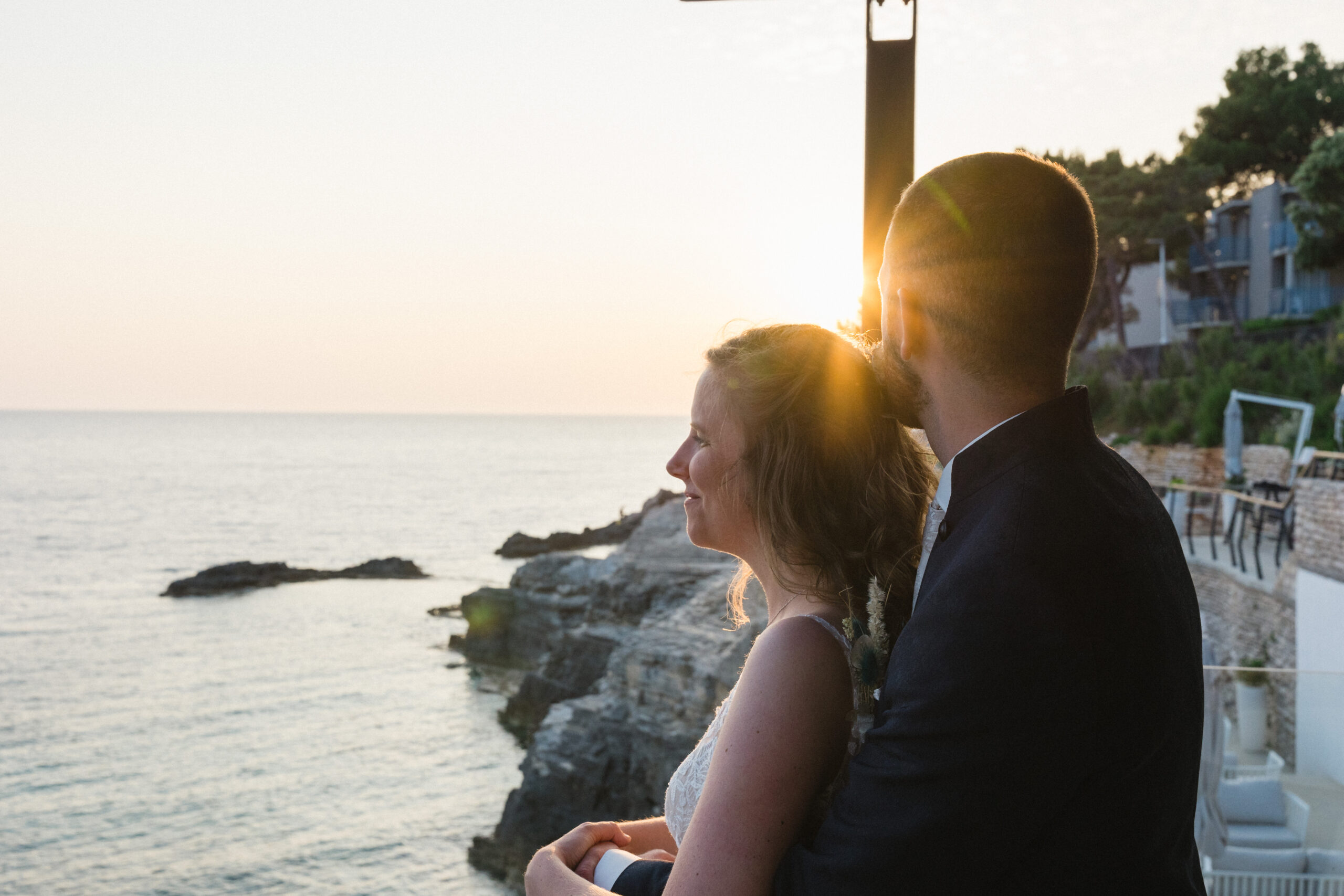 Romantic bride and groom embrace during sunset on a rocky beach in Pula, Istria, Croatia, captured by a wedding photographer.