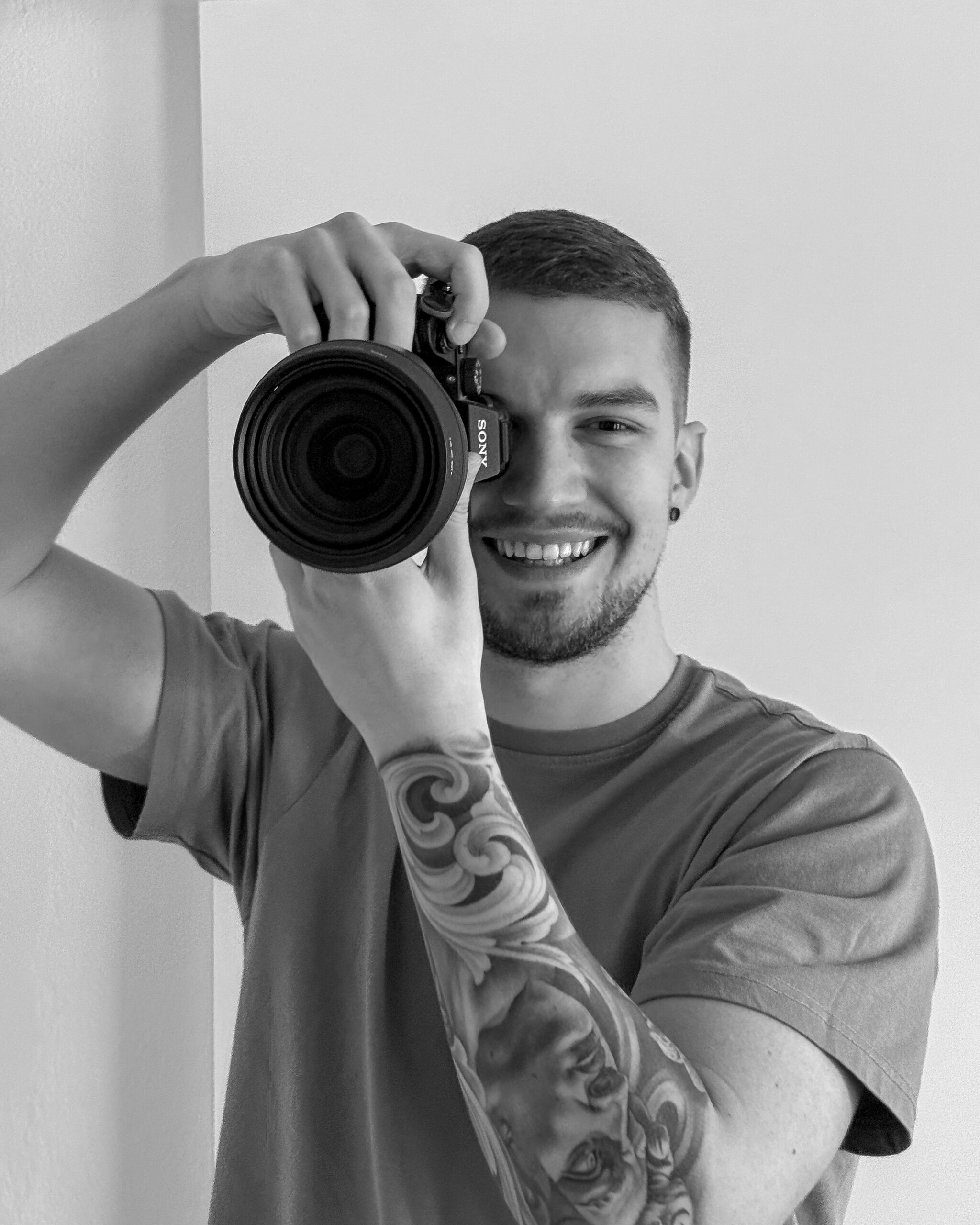 Black and white portrait of Rovinj photographer Dominick Lutrovic holding a Sony camera up to his eye.
